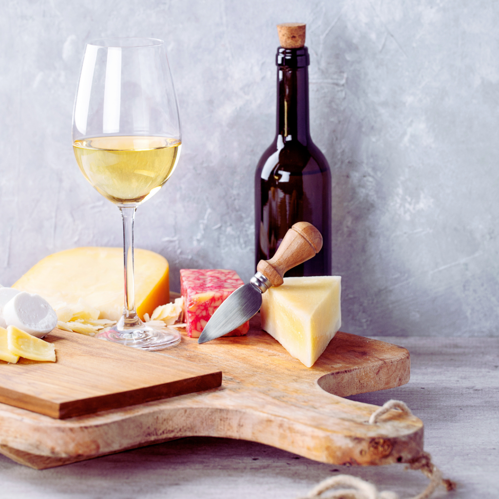 a glass and bottle of wine on top of a cheese board with cheeses.