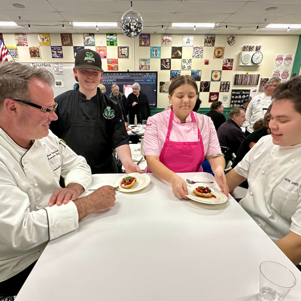 Two high school culinary students serve dinner to two chefs